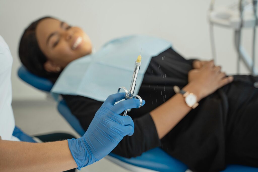 A dentist wearing gloves prepares an injection as a patient smiles in a dental clinic.